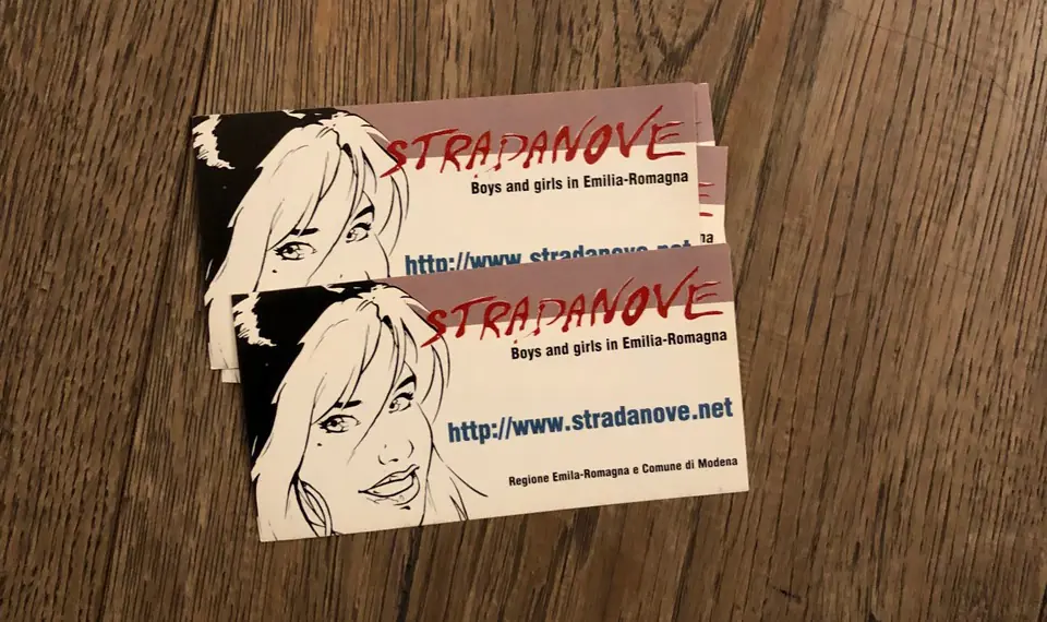 Two business cards introducing Stradanove.net rest on a wooden surface, featuring a comic-style illustration of a woman representing the Emilia-Romagna youth platform.
